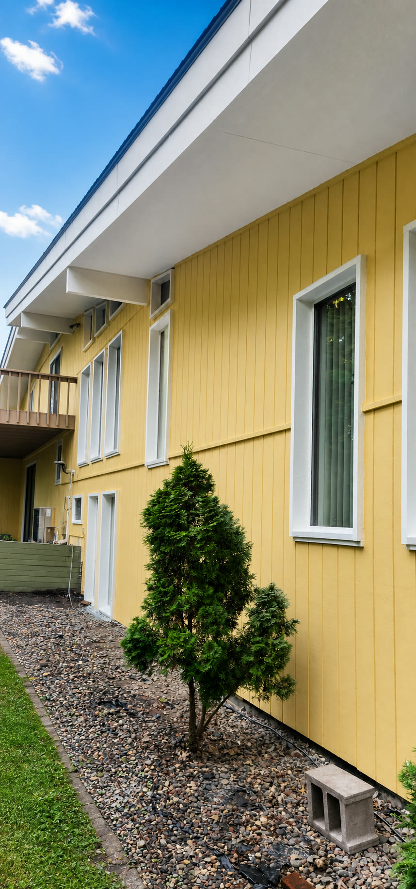 Tom Builders exterior improvement featuring finished yellow siding, white trim, soffits, and windows