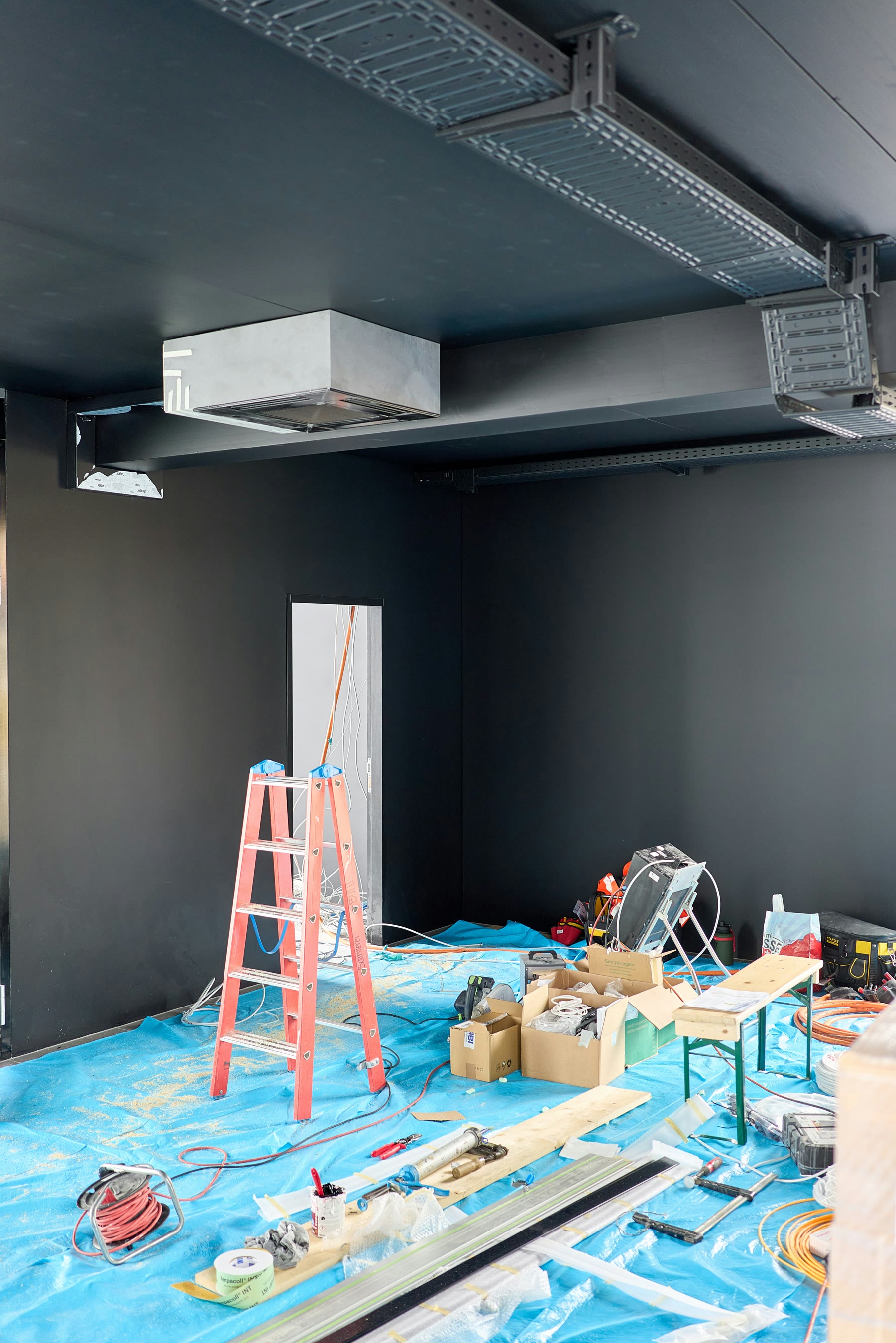 Interior renovation worksite with ladders, tools, materials, and active improvements